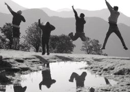 4 people jump simultaneously and show victory signs against a backdrop of mountains.